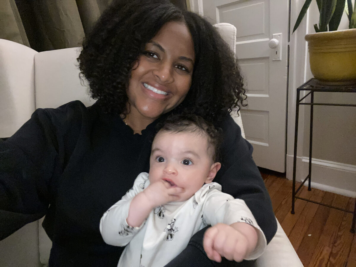 Director Solianna Meaza sit on an armchair, cuddling her baby and smiling at the camera